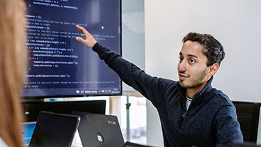 Male student showing programing code on the desktop screen