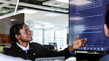 Male student showing programing code on the desktop screen